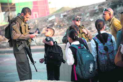 Palestinian child stopped by Israeli soldier ti check his ID.