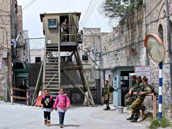 Palestinian children across Israeli check point with armed soldier staring at them
