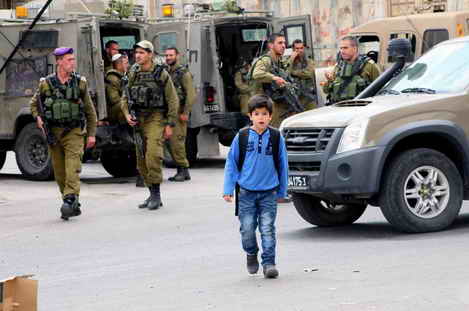 Palestinian child wlaking through Israeli soldiers