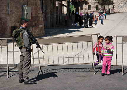 Palestinian children across Israeli check point with armed soldier staring at them