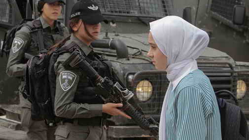 Palestinian girl student across armed Israeli women soldiers